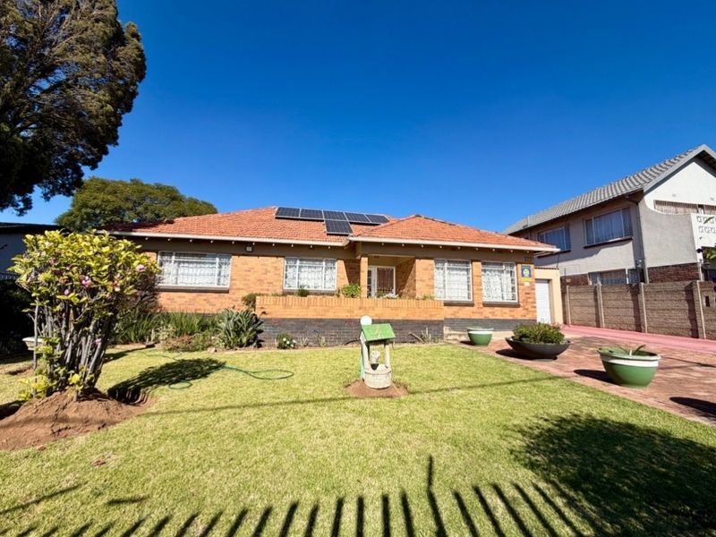 Front view of a single-story brick house featuring a tiled roof, installed solar panels, a well-maintained front lawn, and a paved driveway.