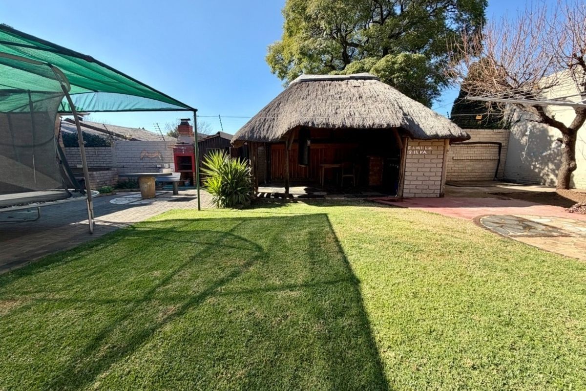 Spacious rear garden featuring a traditional thatched lapa, built-in brick braai, and paved entertainment area, perfect for outdoor living.