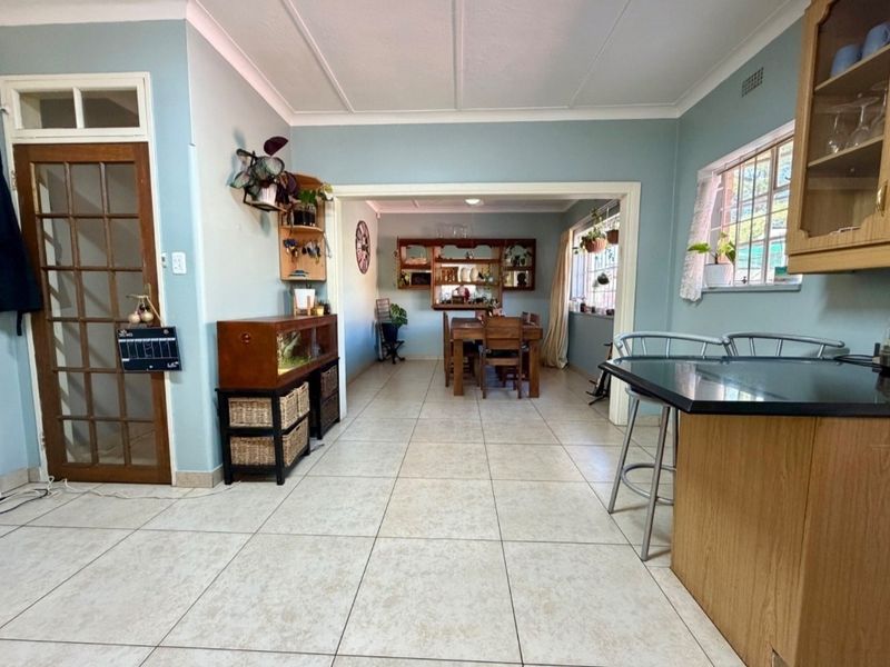 Open plan kitchen and dining area featuring tiled flooring, timber cabinetry, and a breakfast bar, connecting to a secondary living or dining space.
