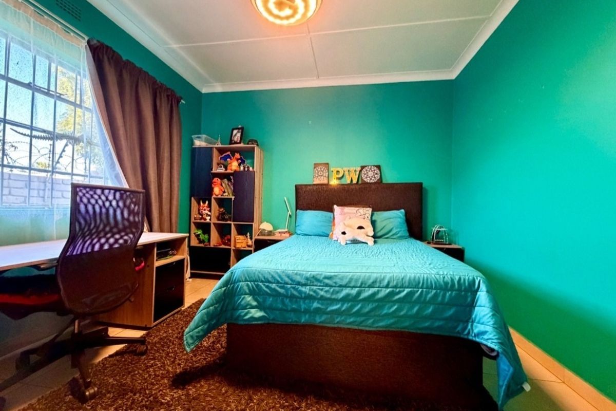 A bedroom featuring bright teal walls, tiled flooring, and a window fitted with security bars.