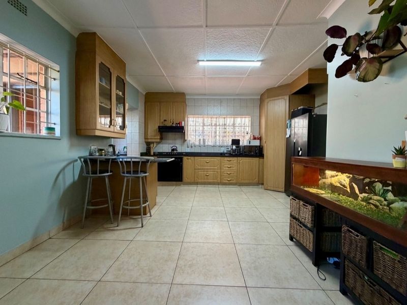 A functional kitchen featuring built-in wooden cabinetry, tiled flooring, a breakfast counter, and a tiled backsplash with integrated oven and extractor fan.