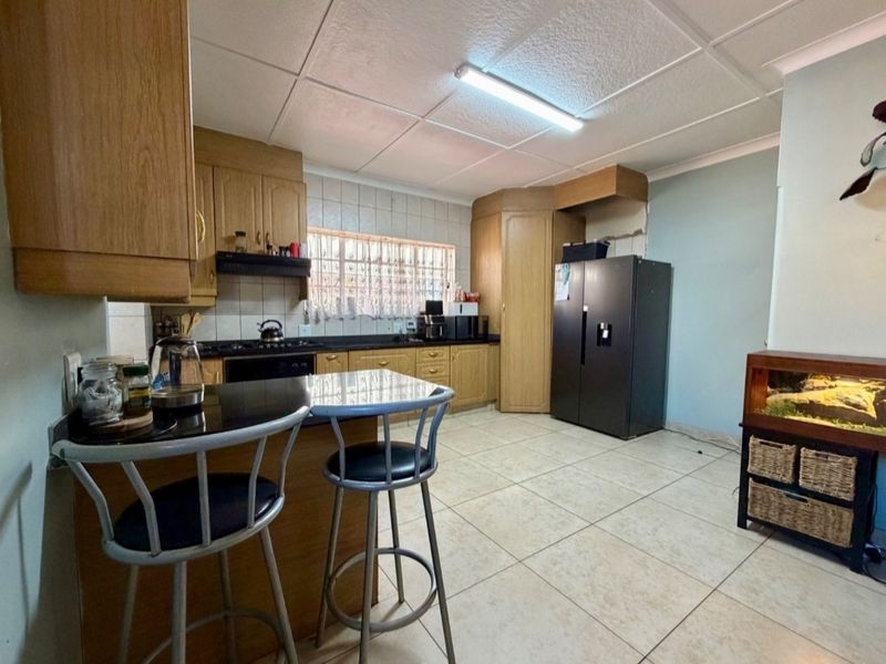 A functional kitchen featuring wooden cabinetry, granite countertops, a breakfast nook, and tiled flooring, requiring some cosmetic updates to the ceiling and wall finishes.