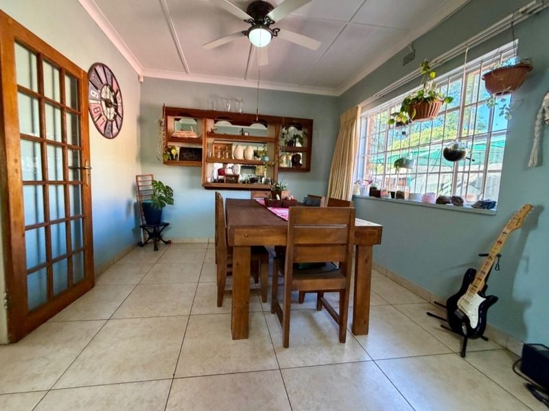 A dining room featuring tiled flooring, a ceiling fan, built-in wall shelving, and a large window providing natural light.