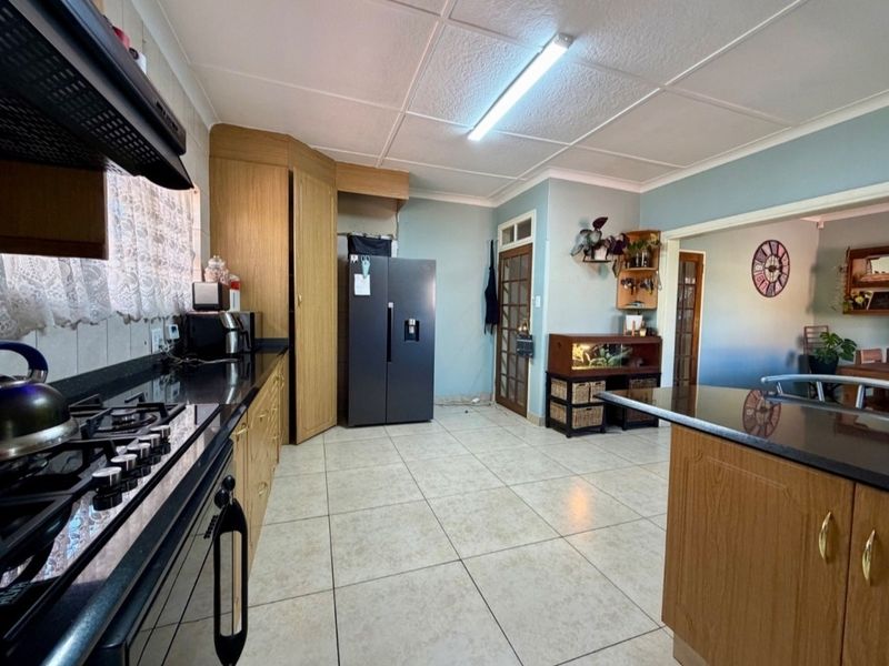A functional kitchen featuring wooden cabinetry, granite countertops, a gas hob with extractor fan, and tiled flooring, offering a practical layout for daily use.