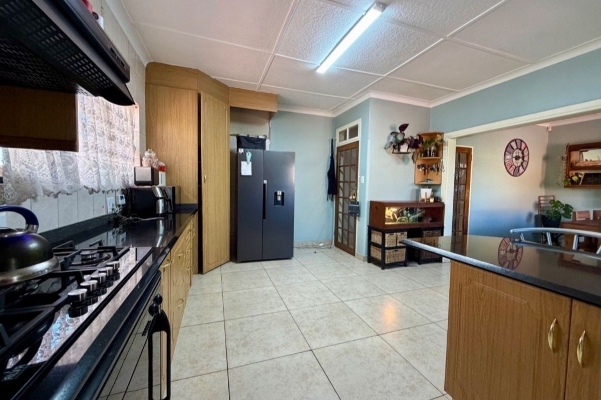 A functional kitchen featuring wooden cabinetry, granite countertops, a gas hob with extractor fan, and tiled flooring, offering a practical layout for daily use.