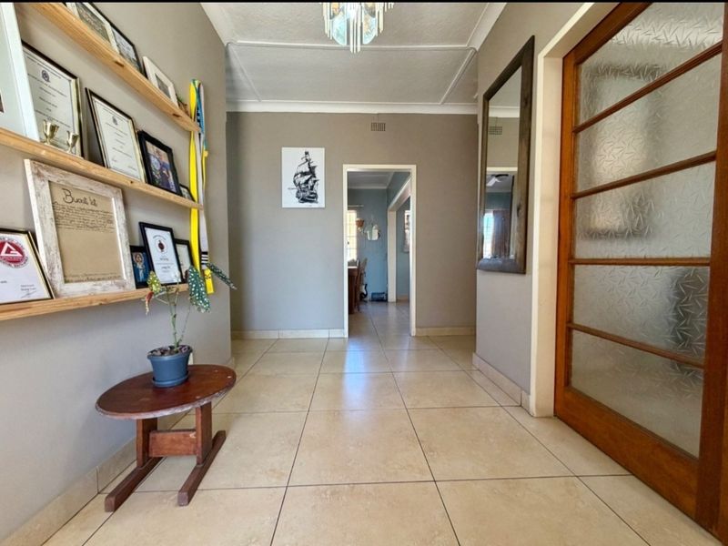A well-maintained hallway featuring neutral tiled flooring, a timber-framed glass door, and classic ceiling cornicing, providing a clean transition between living spaces.