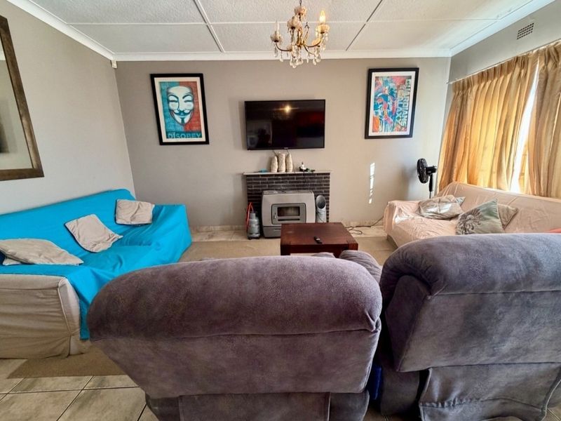 A living room featuring a brick fireplace, tiled flooring, and ceiling tiles, offering a functional space with potential for modernization.
