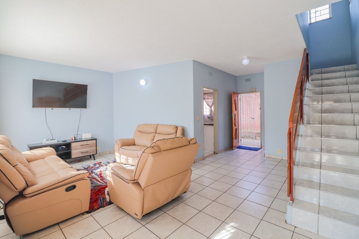 Open-plan living area featuring tiled flooring, a staircase with a wooden handrail, and direct access to the exterior via a security gate.