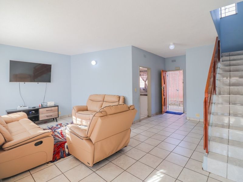 Open-plan living area featuring tiled flooring, a staircase with a wooden handrail, and direct access to the exterior via a security gate.
