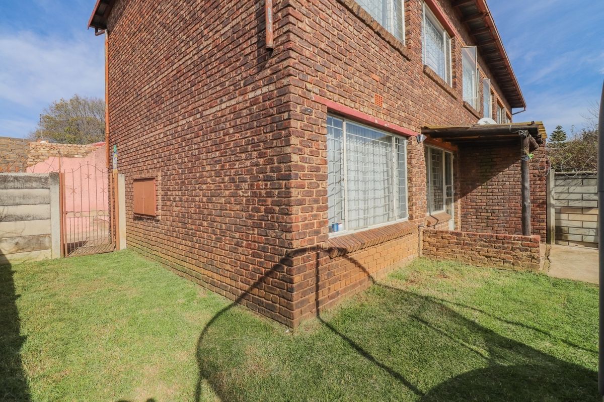 Rear view of a face brick townhouse featuring a small garden, security bars on windows, and a covered patio area.