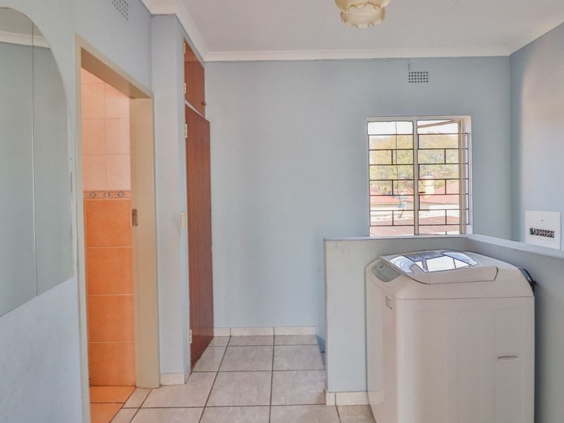 A functional laundry area featuring tiled flooring, built-in storage cupboards, and a window with security bars, providing a practical utility space.