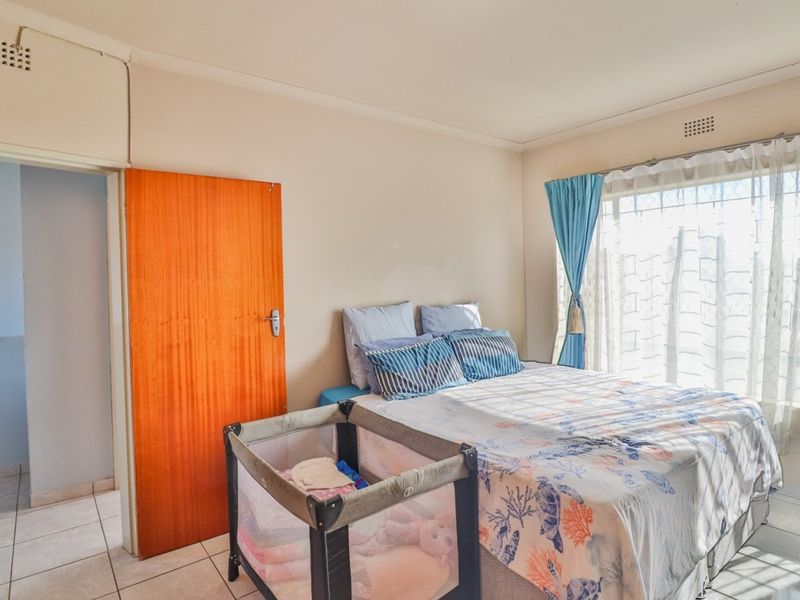 A functional bedroom featuring tiled flooring, a built-in door, and a window fitted with security bars for added peace of mind.