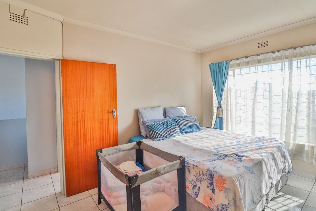 A functional bedroom featuring tiled flooring, a built-in door, and a window fitted with security bars for added peace of mind.