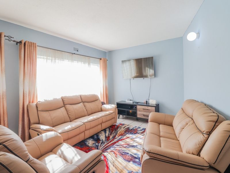 A comfortable living room featuring tiled flooring, a wall-mounted light fixture, and a large window allowing for natural light.