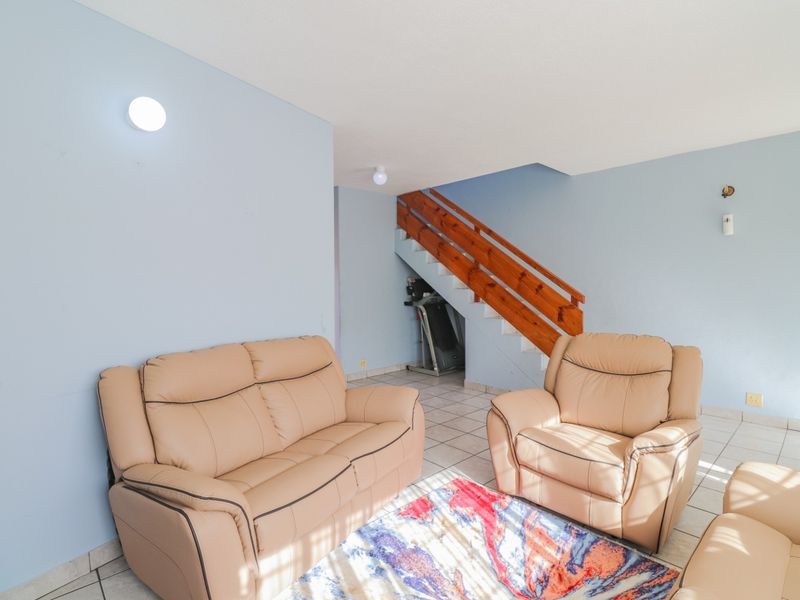 A living room area featuring tiled flooring and a staircase with a wooden handrail, providing access to the upper level of the townhouse.