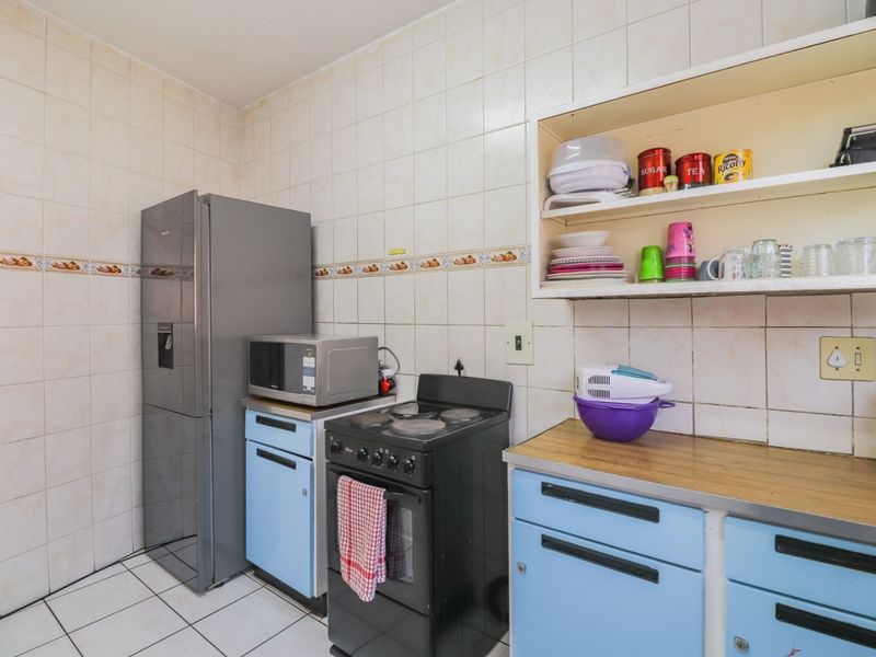 A functional kitchen featuring tiled walls and flooring, built-in cabinetry with laminate countertops, and a freestanding stove, offering potential for modern updates.