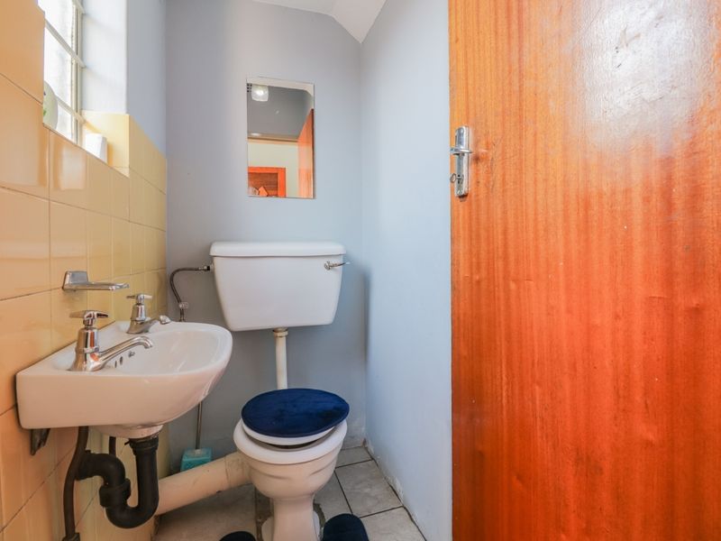 A compact guest bathroom featuring a wall-mounted basin, ceramic toilet, and dated yellow wall tiling with exposed plumbing fixtures.