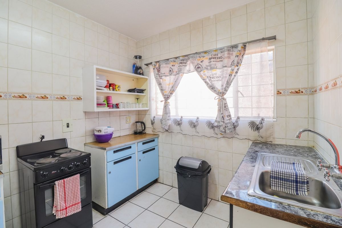 A functional kitchen featuring a freestanding stove, stainless steel sink, and ample wall tiling, offering a dated aesthetic ready for modernization.