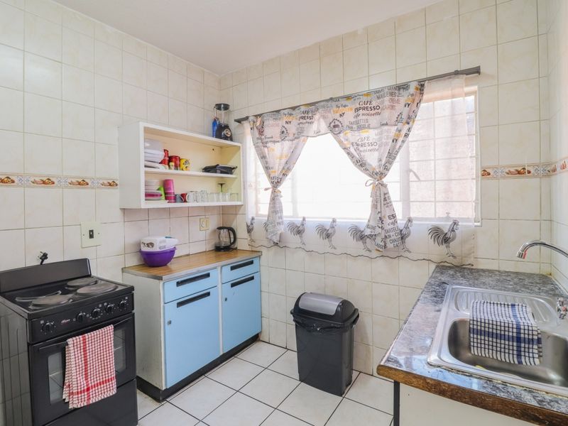 A functional kitchen featuring a freestanding stove, stainless steel sink, and ample wall tiling, offering a dated aesthetic ready for modernization.