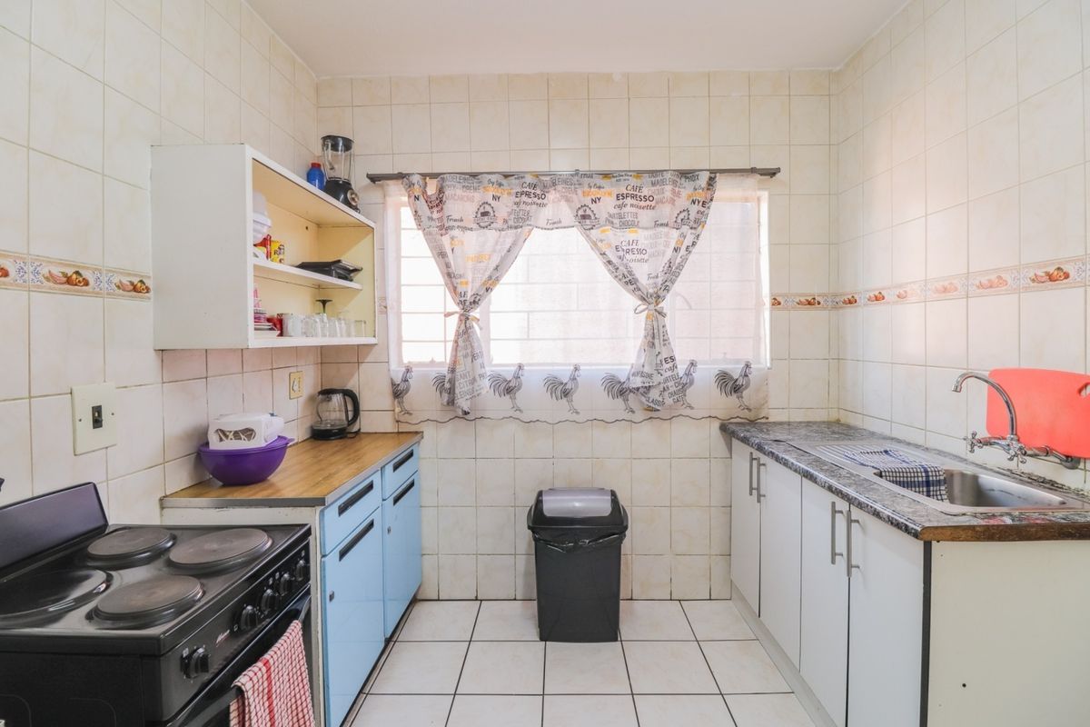 A functional kitchen featuring tiled walls and floors, built-in cabinetry, and a stainless steel sink, offering potential for a modern renovation.