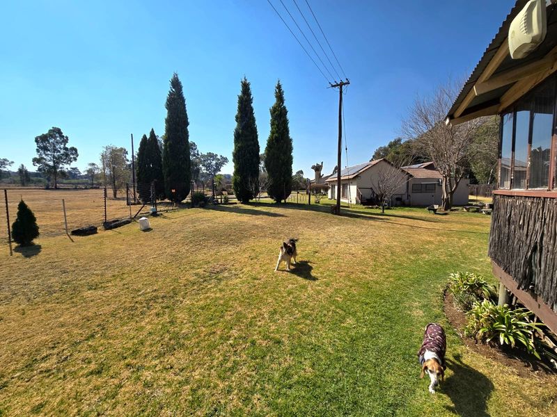 Spacious garden area featuring established trees, perimeter fencing, and a view of the property's exterior structure with timber cladding and corrugated roofing.
