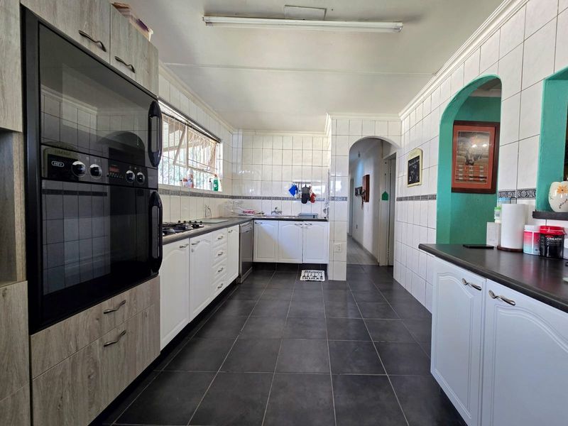 A functional kitchen featuring built-in oven, gas hob, tiled backsplash, and ample cabinetry with dark tiled flooring and arched entryways.