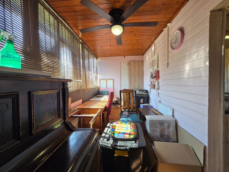 Enclosed patio area featuring a timber tongue and groove ceiling, ceiling fan, and timber wall cladding, currently utilized as a multi-purpose storage and workspace.