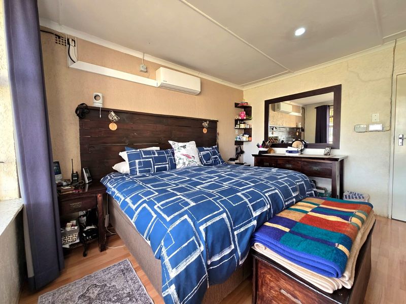 A bedroom featuring laminate flooring, an air conditioning unit, and a built-in wall mirror, showing signs of dated finishes and surface-mounted electrical wiring.