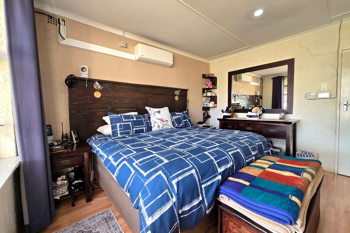 A bedroom featuring laminate flooring, an air conditioning unit, and a built-in wall mirror, showing signs of dated finishes and surface-mounted electrical wiring.
