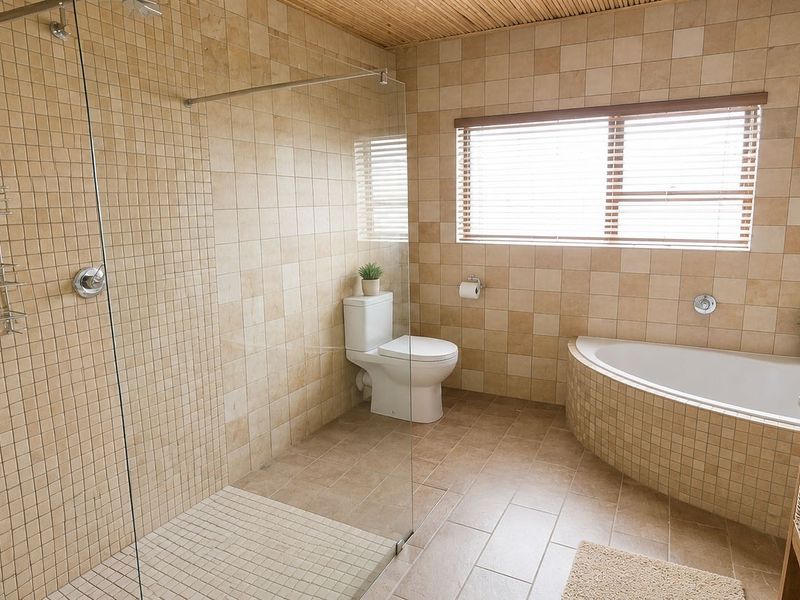 A well-maintained bathroom featuring a walk-in shower with glass screen, a built-in bathtub, a vessel sink, and neutral tiled finishes throughout.