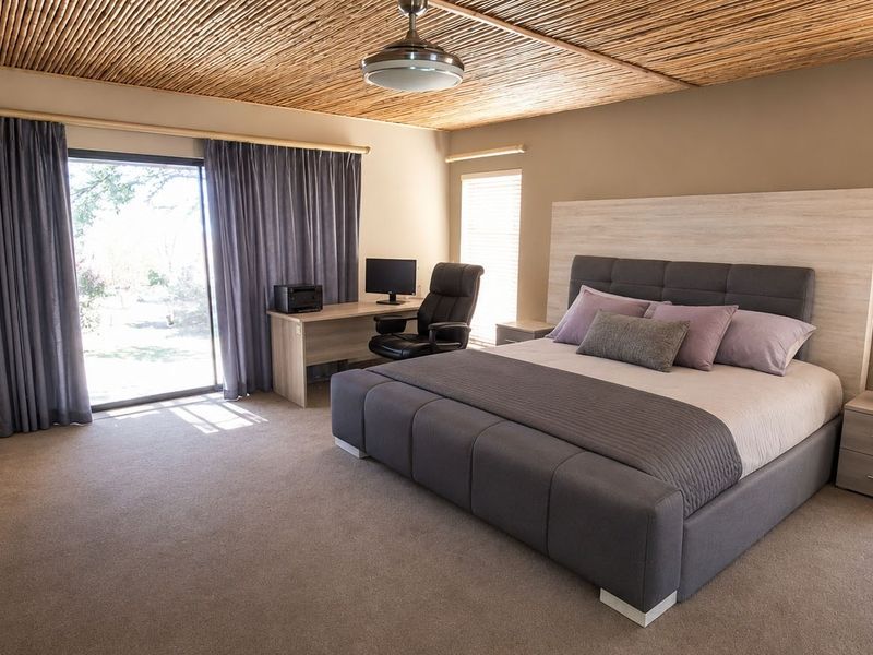 Spacious bedroom featuring a unique thatched ceiling, ceiling fan, carpeted flooring, and built-in cupboards with direct access to the garden through a sliding door.