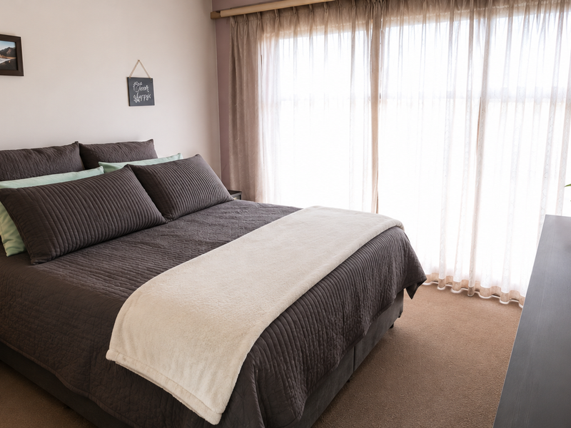A well-maintained bedroom featuring neutral carpeting and a large sliding glass door with sheer curtains, providing ample natural light.