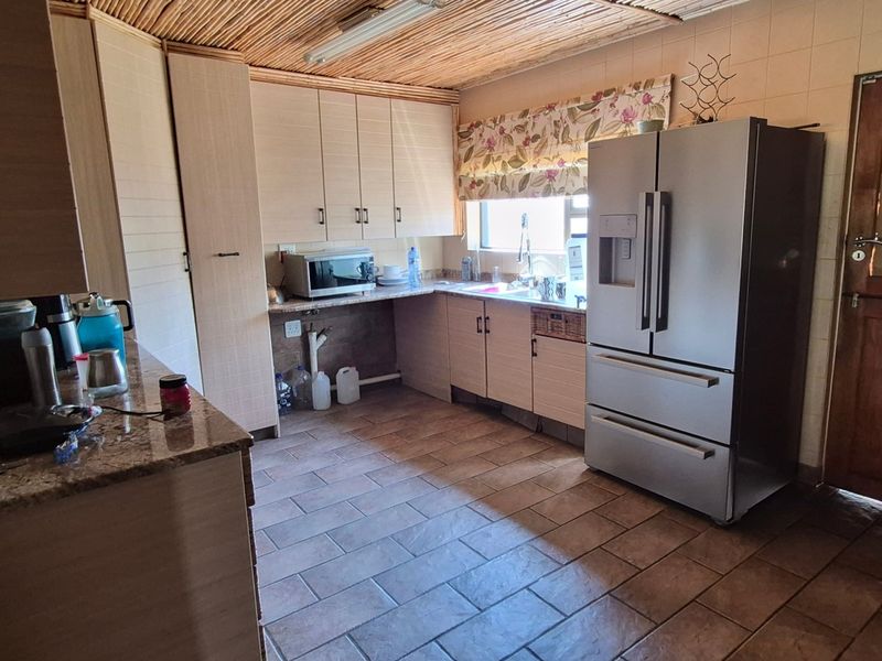 A functional kitchen featuring built-in cabinetry, granite countertops, tiled flooring, and a unique thatched ceiling, providing a rustic aesthetic.