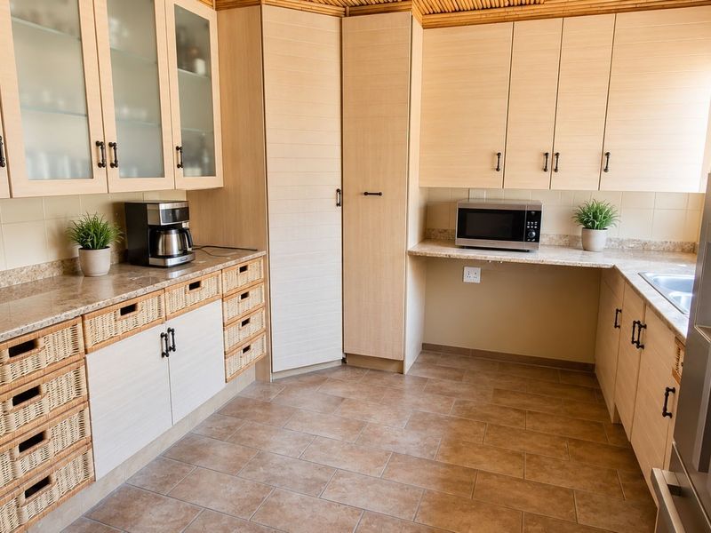 A well-maintained kitchen featuring light wood-finish cabinetry, integrated microwave, stone-look laminate countertops, and durable tiled flooring.