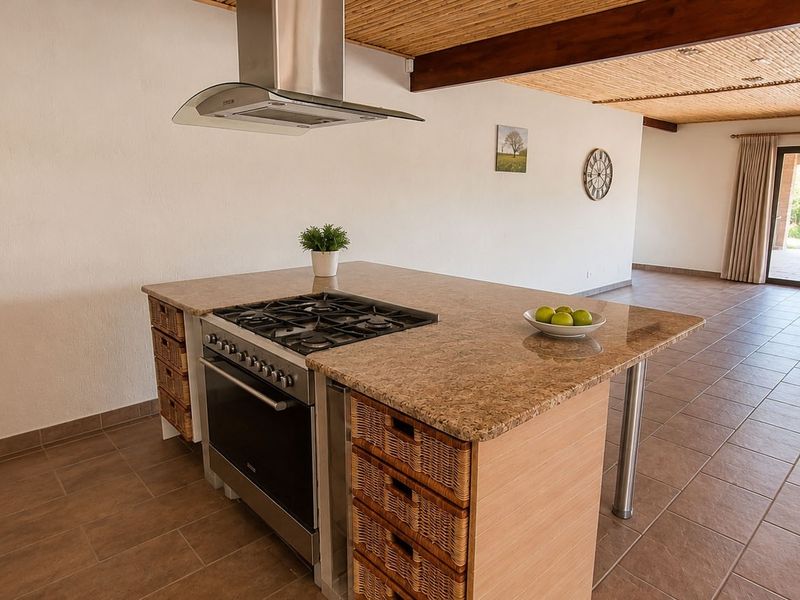 Spacious open-plan kitchen featuring a central island with granite countertops, gas hob, and built-in oven, complemented by a unique bamboo ceiling and tiled flooring.