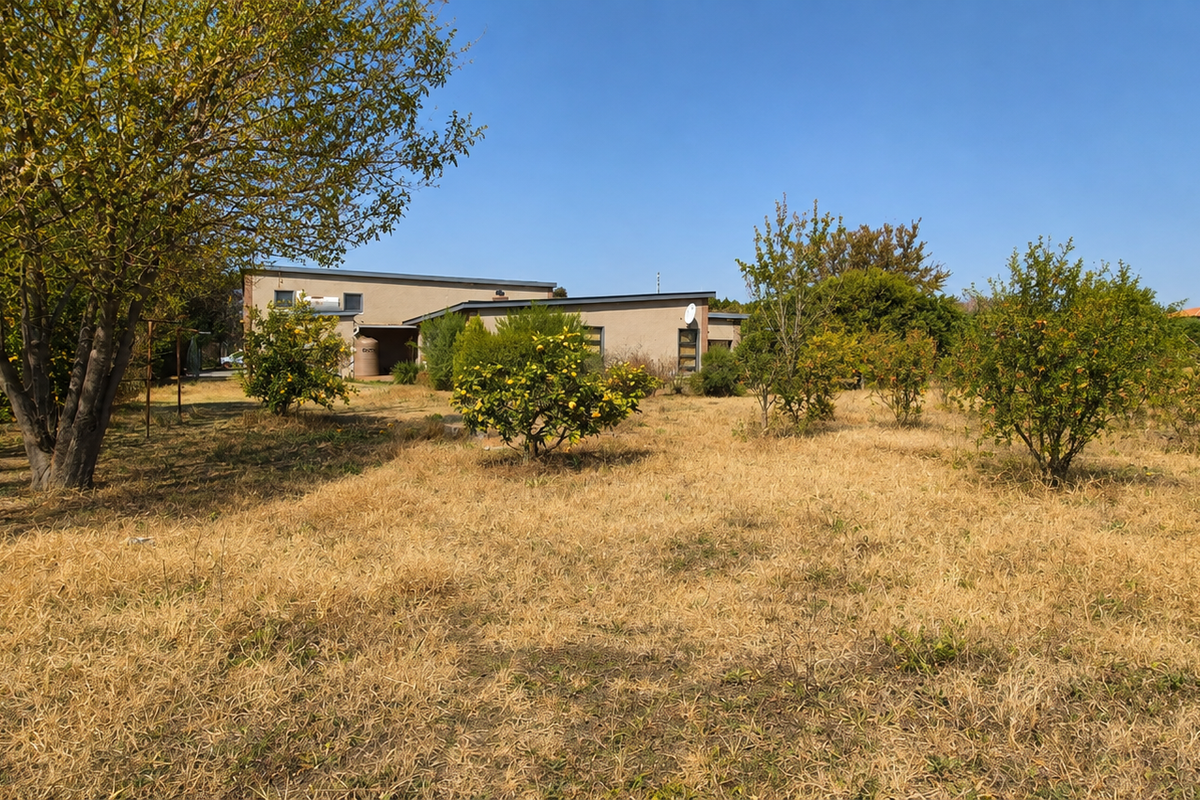 A view of the rear exterior of the property featuring a large garden area with mature trees, fruit trees, and a water storage tank.