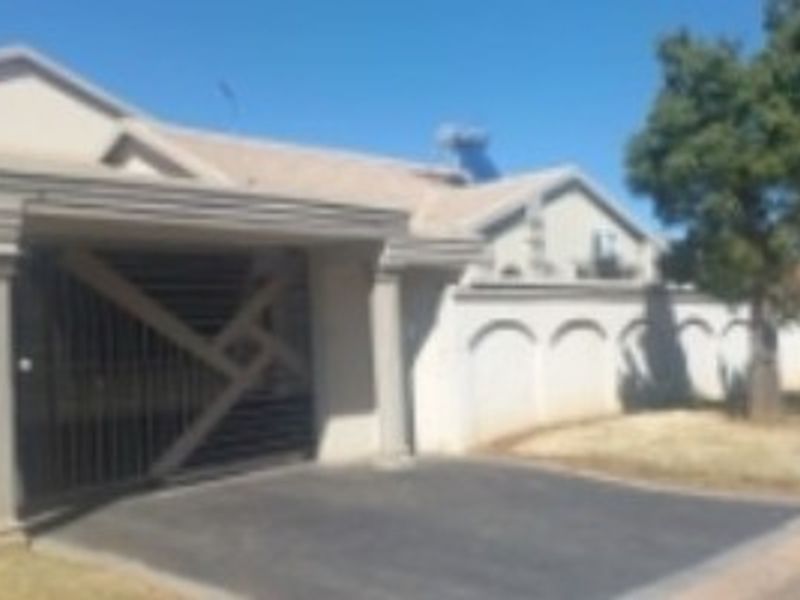 Front exterior view of the property featuring a paved driveway, security gate, and perimeter wall with a solar geyser installed on the roof.