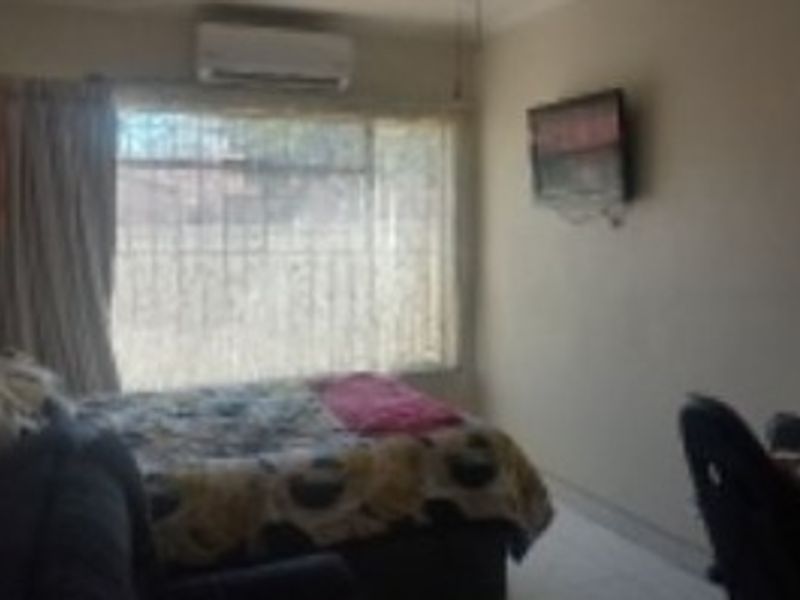 A functional bedroom featuring tiled flooring, a wall-mounted air conditioning unit, and security bars on the window.
