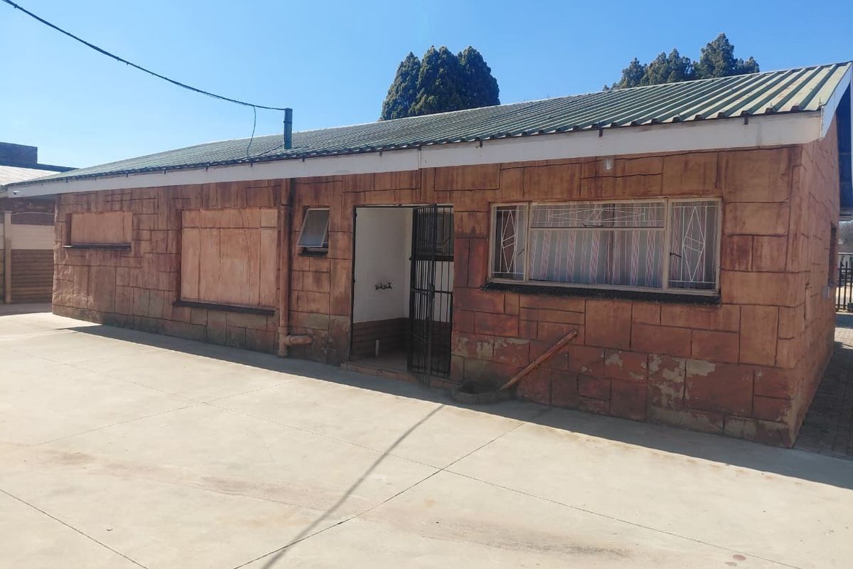 Rear exterior view of a single-story house featuring a stone-clad facade, corrugated metal roof, and concrete driveway area.