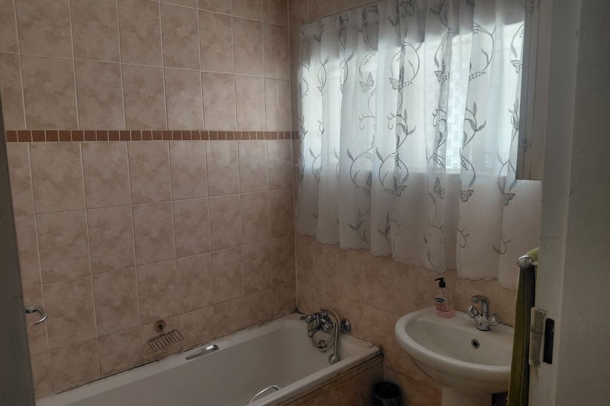 A functional bathroom featuring a bathtub, pedestal basin, and neutral wall tiling, offering a classic layout ready for modern updates.