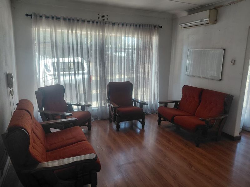 A living room featuring laminate flooring and a wall-mounted air conditioning unit, currently showing signs of wear on the wall finishes.