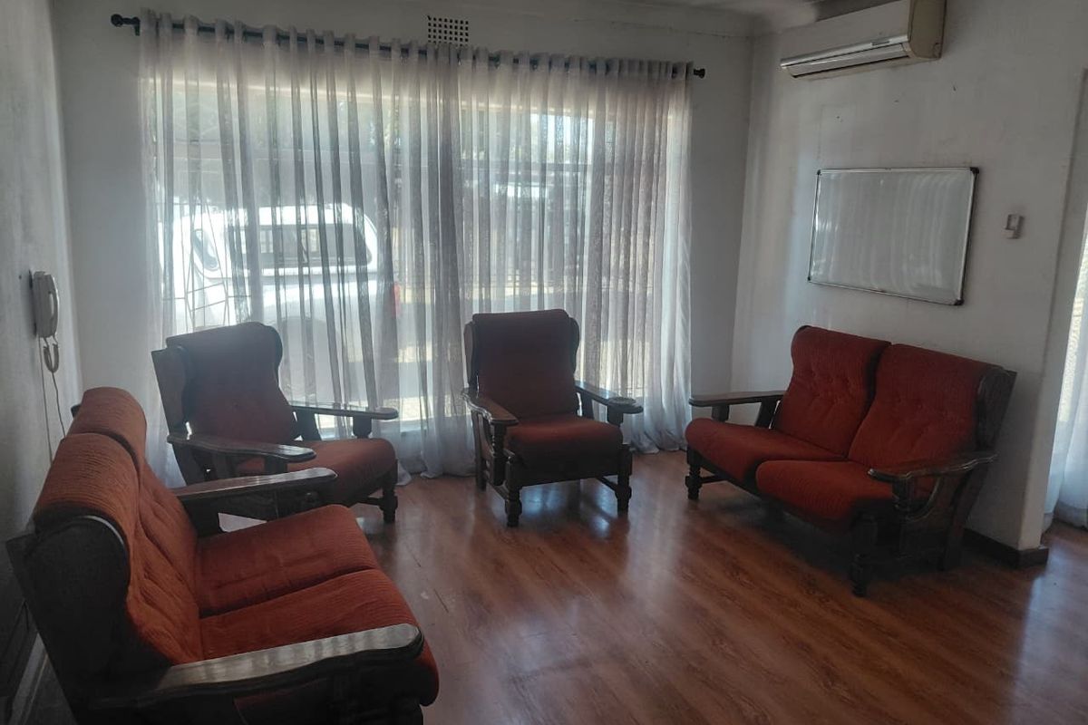 A living room featuring laminate flooring and a wall-mounted air conditioning unit, currently showing signs of wear on the wall finishes.