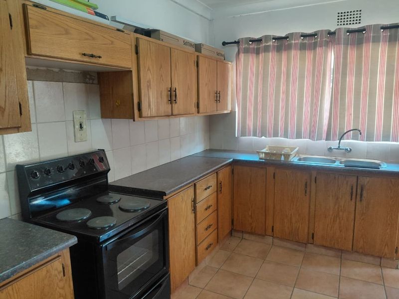 A functional kitchen featuring wooden cabinetry, laminate countertops, a double basin sink, and ceramic tile flooring, offering potential for modern updates.