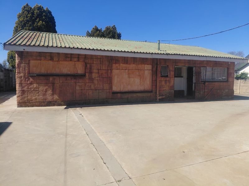 Front exterior view of a single-story house featuring stone cladding, a corrugated metal roof, and a large concrete driveway area.