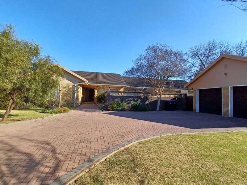 Front view of a residential property featuring a spacious paved driveway, a double garage, and a well-maintained garden area.