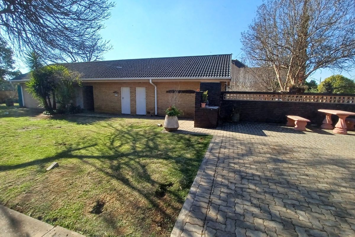 Rear exterior view featuring a paved patio area, built-in braai, brick boundary wall, and a spacious lawn.