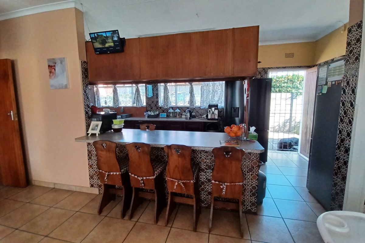 A dated kitchen featuring a breakfast bar, tiled counters, and built-in cabinetry with direct access to the exterior through a security gate.