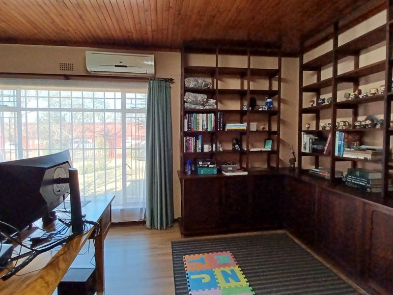 Home office featuring extensive built-in wooden shelving, timber-clad ceiling, laminate flooring, and a wall-mounted air conditioning unit.