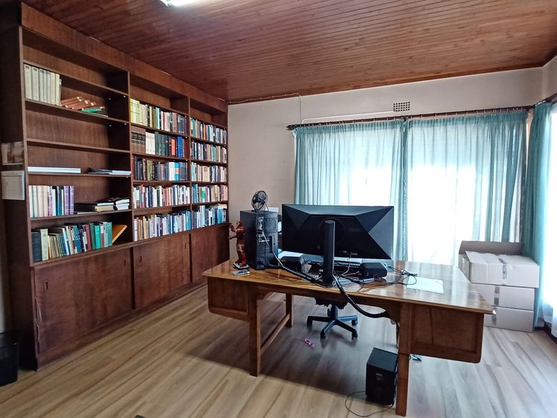 A home office featuring a large built-in wooden bookshelf, timber ceiling, and laminate flooring, providing a functional workspace with ample storage.