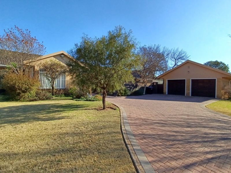 Front view of a residential property featuring a paved driveway, a double garage, and a well-maintained garden area.